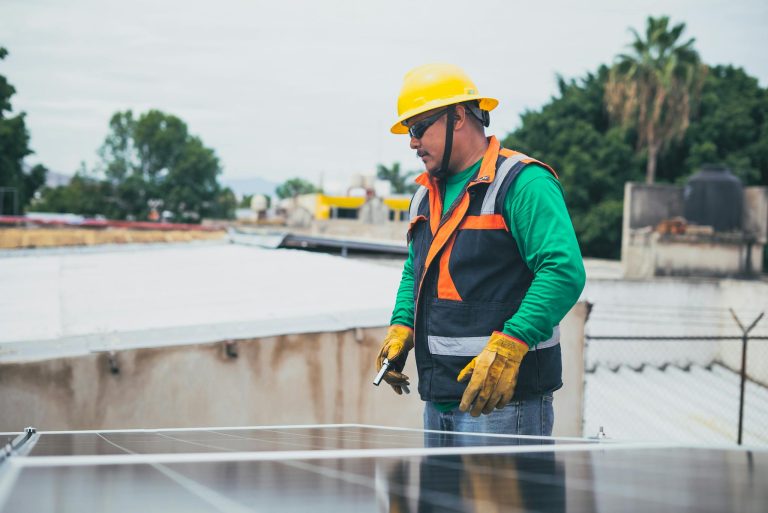 A solar technician in protective gear inspecting rooftop solar panels outdoors.